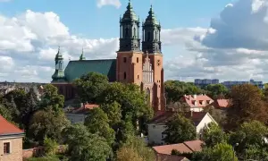 Bazylika archikatedralna świętych apostołów Piotra i Pawła w Poznaniu, majestatyczna budowla z cegły z zielonym dachem, góruje nad drzewami i domami.