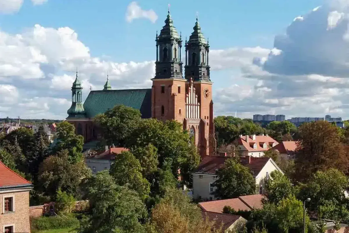 Bazylika archikatedralna świętych apostołów Piotra i Pawła w Poznaniu, majestatyczna budowla z cegły z zielonym dachem, góruje nad drzewami i domami.