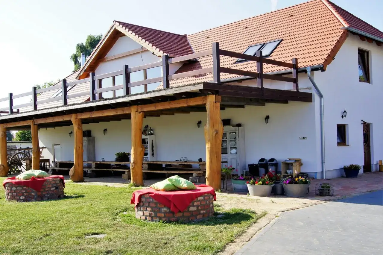 Urokliwa farma zwierząt z werandą i miejscami do siedzenia na trawie. Drewniane belki i ceglane paleniska tworzą rustykalny klimat.