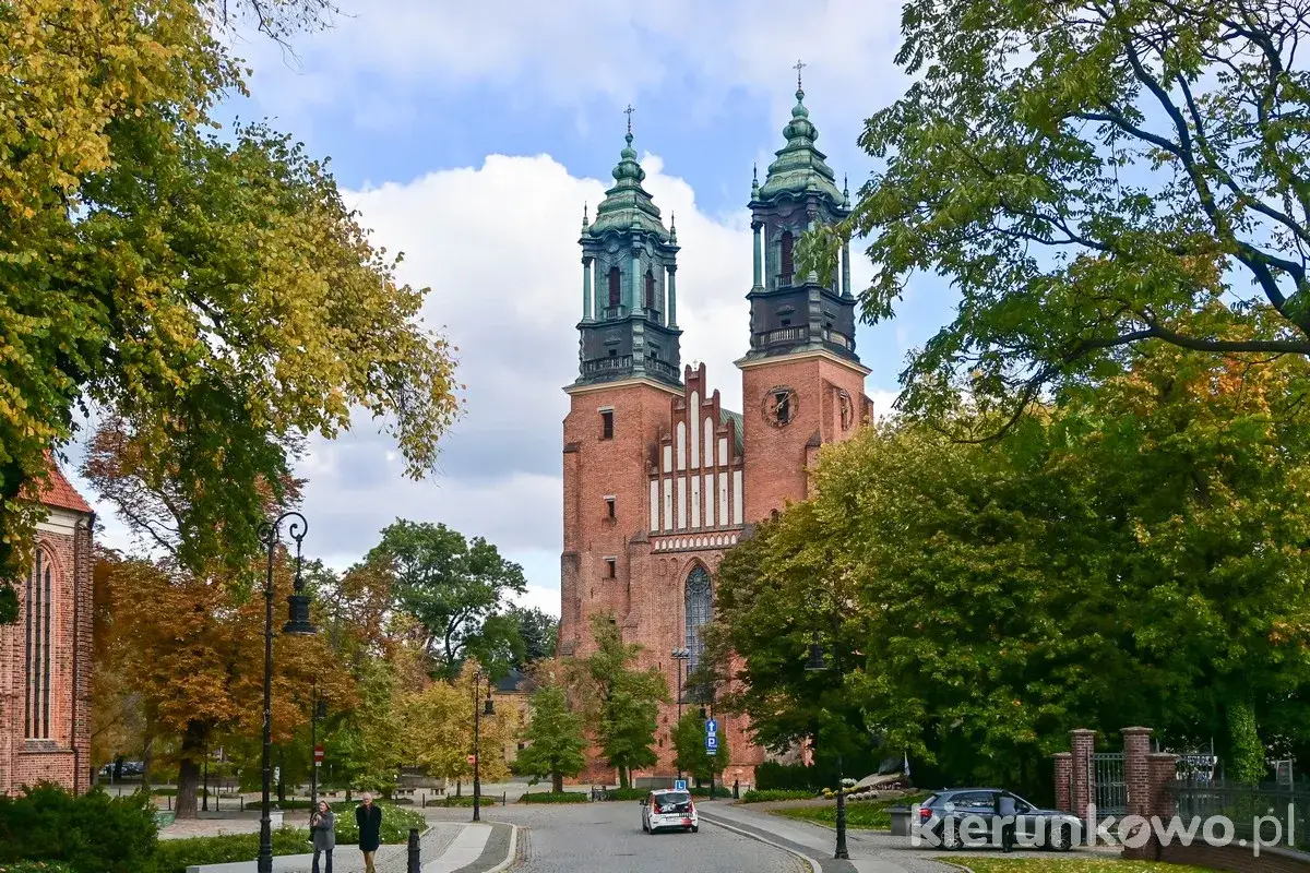Jesienna panorama Poznania z bazyliką archikatedralną świętych apostołów Piotra i Pawła w tle, otoczoną kolorowymi drzewami.