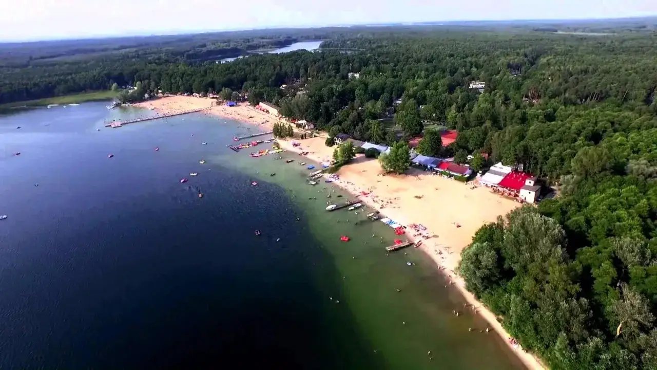 Widok z lotu ptaka na plażę i jezioro w Skorzęcinie. Tłumy ludzi odpoczywają na piasku, pływają i korzystają z wodnych atrakcji. To prawdziwy diament wśród polskich kurortów.